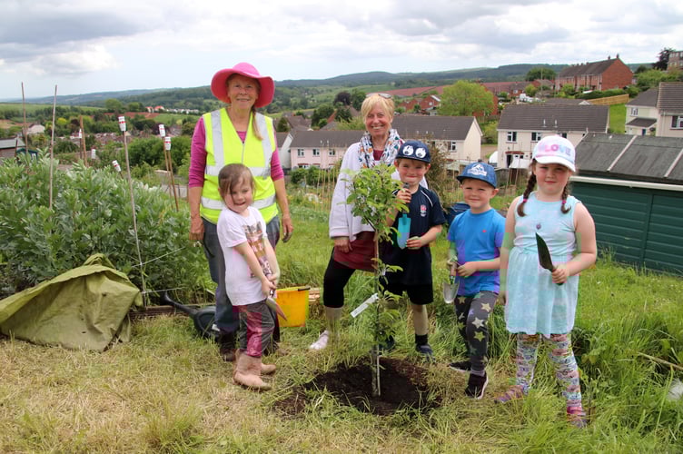 Christina Dymond, left, with Bridget Merritt, centre, with the children who enjoyed planting an apple tree.  AQ 6445
