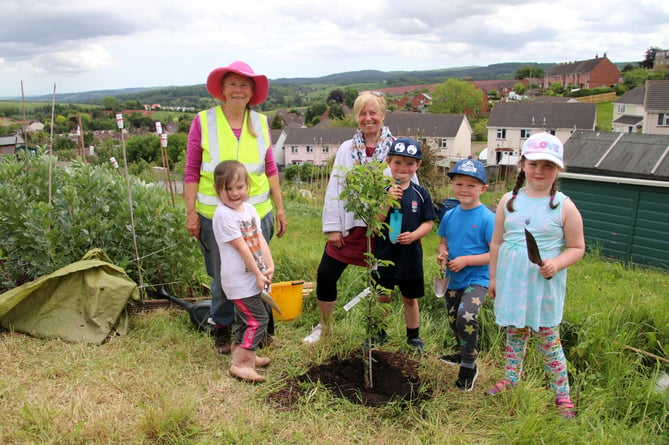 Christina Dymond, left, with Bridget Merritt, centre, with the children who enjoyed planting an apple tree.  AQ 6445
