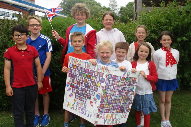 Children dressed in red, white and blue at Bow Community Primary School to celebrate the Queen’s Platinum Jubilee before half-term.  Pictured are some of the children with the card for the Queen which all the children at the school contributed to or signed.
