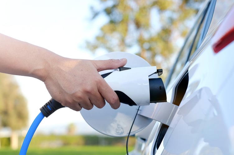 Electric car or ev is charging at station . man use the white power cable and plug on nature background. eco and clean energy concept with the mobile phone smart technology. zero gas and no transmission.