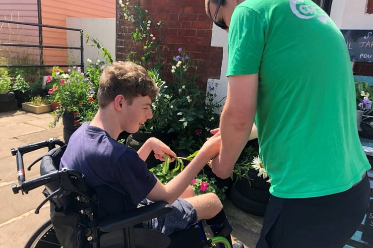 A charity worker at The Turning Tides Project assisting a young boy in the garden.
