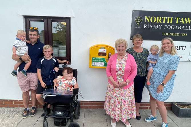 Mrs Newstead, centre right, with members of her family and the defibrillator on the side of North Tawton RFC clubhouse.  AQ 1242