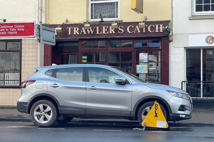 The Nissan car parked in Crediton High Street with its bright yellow clamp. AQ 9552