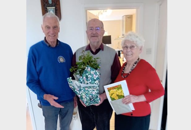 Crediton Boniface Rotary President Garry Adams, left, presenting a rose bush to Reuben Miles, his wife, Heather holding a picture of the rose in bloom.

