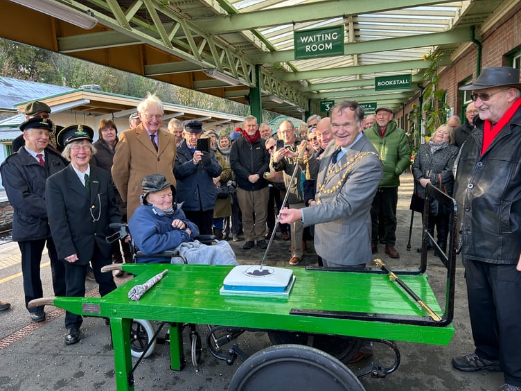 Okehampton mayor Allenton Fisher cuts the Dartmoor Line 3rd birthday cake with his ceremonial navy sword, watched by all those who helped the railway return to the town