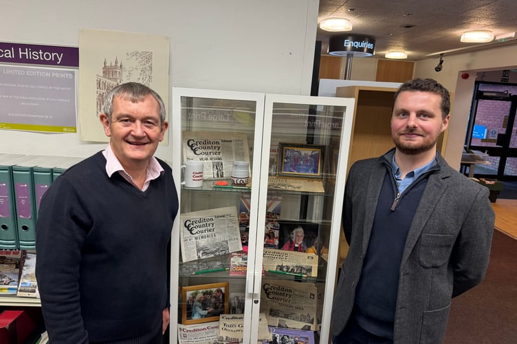 Courier Editor Alan Quick, left and Reporter Will Goddard, in front of the display cabinet of items to mark 50 years of the Crediton Courier at Crediton Library.  
