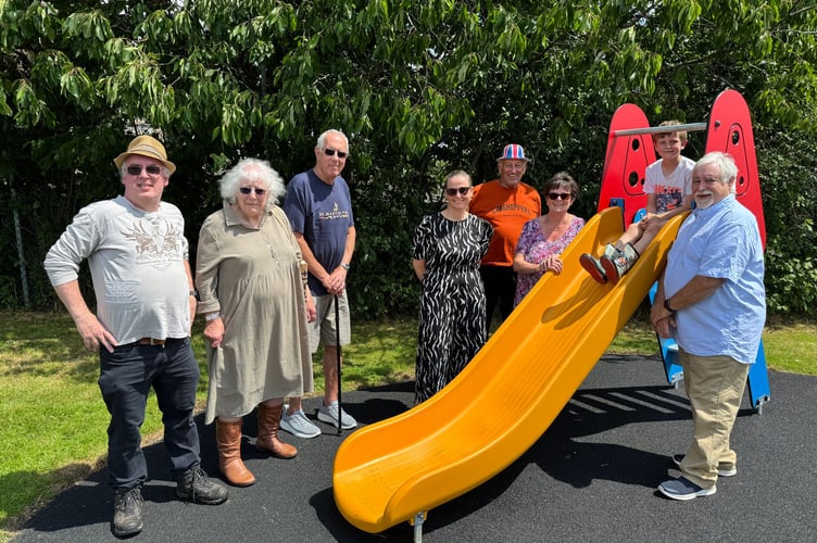 Beside one of the new items of play equipment at Lapford, from left, Cllr Steve Fletcher, Cllr Sue Briant-Evans, Cllr Bill Graham, Mrs Jess Wright, Head of Lapford School, Cllr Roy Andrews, Chairman Cllr Julie Down and right County and District Councillor Steve Keable, a young person on the slide.  AQ 5269

