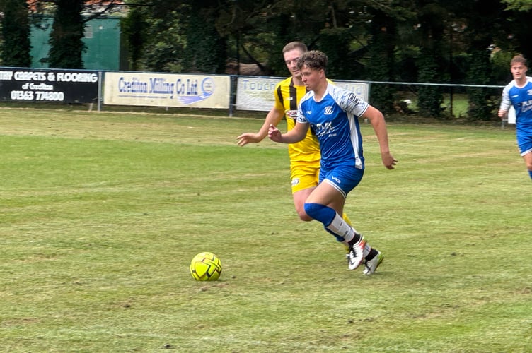 A Crediton United player, in blue, and member of Dave Lee XI battle for the ball. AQ 7119