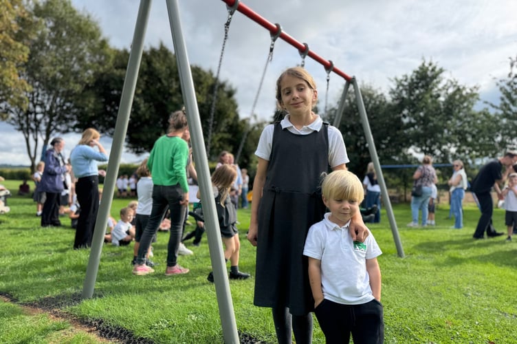 The oldest and youngest schoolchildren at Newton St Cyres Primary School cut a ribbon to open the new swings at the Recreation Ground.  AQ 3253
