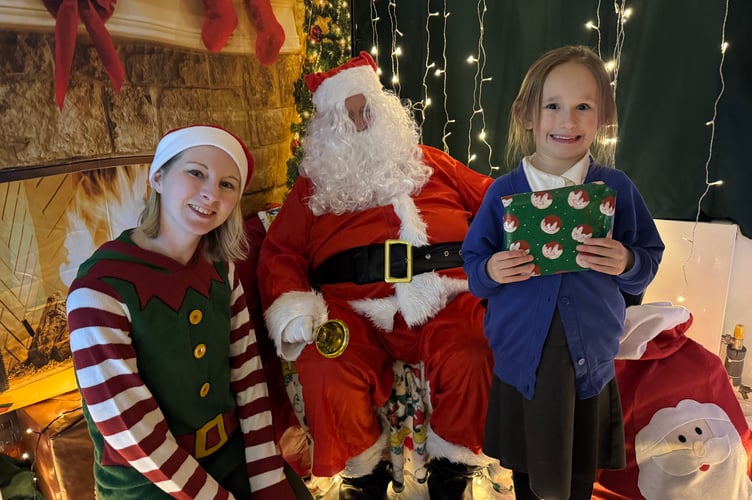 Father Christmas and his helper with a young visitor with her gift at Bow School. AQ 9994