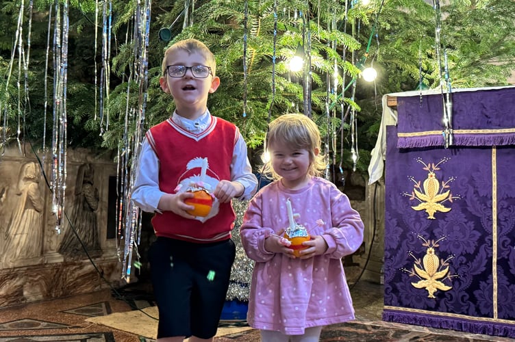 In front of the giant tree in Crediton Parish Church, two youngsters with their Christingles.  AQ 0642
