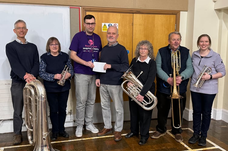 Crediton Town Band chairman Chris Richards, centre, presents the donation in memory of former band MD Chris Taylor to Tom Darby-Clark, with Mrs Margaret Taylor, centre right, with some of the other band members.  AQ 4821
